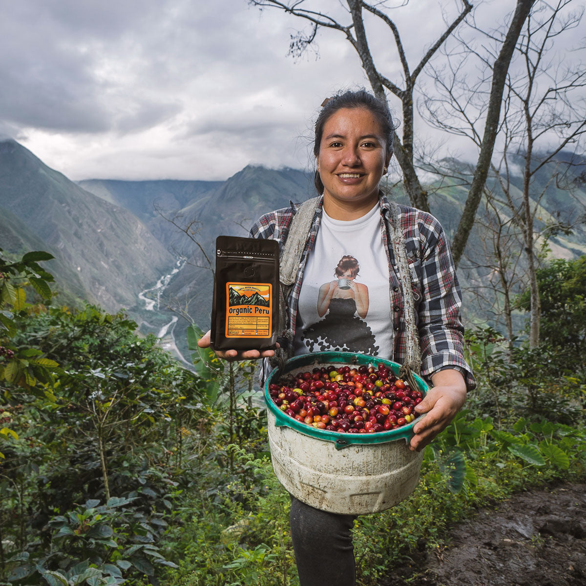 Peruvian coffee farmer holding unprocessed coffee cherries and a 12oz bag of Organic Peru coffee in front of the mountains
